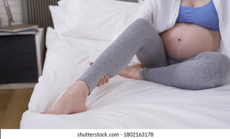 Close Up Mother-to-be Rubbing Her Swelling Leg With Hands On White Bedding.