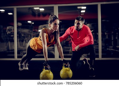 Close up of motivated focused attractive young woman doing push ups exercise on the kettlebells in the gym with her handsome muscular personal trainer. - Powered by Shutterstock