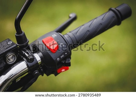 Close up of a motorcycle handlebar with a red engine kill switch and black rubber grip