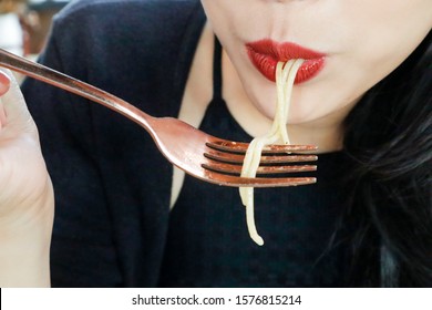 Close Up Of Woman’s Mouth Eating Spaghetti By Using Her Fork. Focus Of A Girl Wearing Red Lipstick Consuming Her Food.