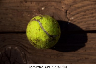 Close Up Of A Muddy Tennis Ball On A Wooden Bench From The Dog Park.