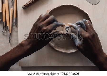 Close up of multicultural craftswoman's hands imprinting and decorating earthenware on pottery class at modern studio. Cropped picture of african american pottery class student decorating earthenware.