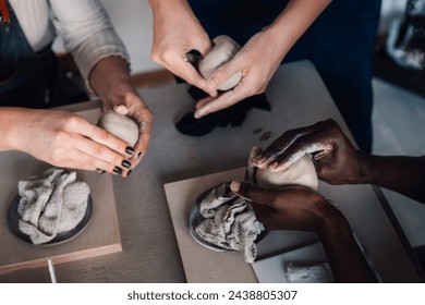 Close up of multicultural pottery class students' hands modeling clay at a pottery workshop.Tutor is showing clay work and clay modeling at pottery masterclass while students learning it.Pottery class - Powered by Shutterstock