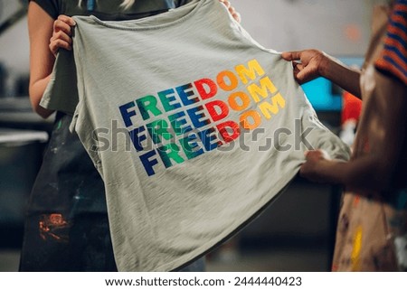 Close up of multicultural printing workshop workers' hands holding silk screen printed t-shirt and promoting lgbtq equality. Cropped picture of multiracial female workers hands holding printed shirt.