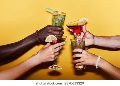 Close up of multiethnic group of people holding cocktail glasses on yellow background and toasting in celebration - Powered by Shutterstock