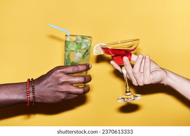 Close up of multiethnic young couple holding two cocktails against vibrant yellow background - Powered by Shutterstock
