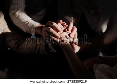 Close up of multiple hands joined together in warm dramatic light. Symbolic moment of friendship, unity and support during wedding celebration.