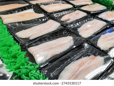 Close up of multiple packaged fish fillets arranged on artificial grass in supermarket seafood section