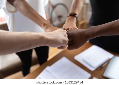 Close up multiracial colleagues bumping fists at meeting. Young mixed race employees engaged in motivating teambuilding process at office. Group of different ethnicities business people showing unity.