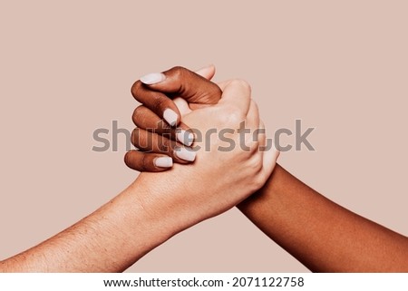 Close up multiracial woman couple with black and caucasian hands holding each other in tolerance unity love and anti racism concept. Studio shot, pastel beige background.