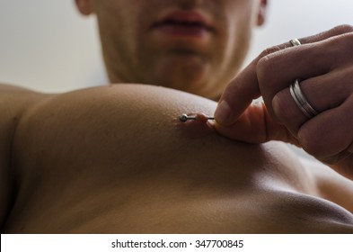 Close up of muscular male torso with hand pulling nipple piercing