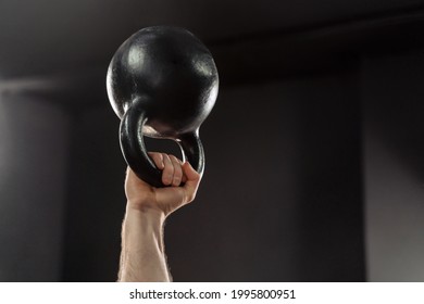 Close Up Of Muscular Man's Hand Holding A Kettlebell Overhead, Doing Weightlifting Exercises At Gym, Isolated On Dark Background. Strong Arm Lifting Kettlebell Overhead During Weight Training Crossfit