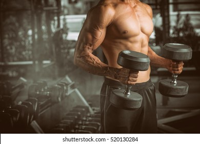 Close Up of a muscular young man lifting weights in gym on dark background.