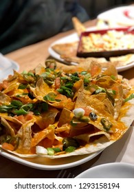 Close Up Of Nacho Platter With Warm Fall Coloured Spinach Dip In Soft Focus In The Background