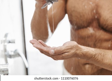 Close up of a naked man putting shower gel from a bottle while having a shower