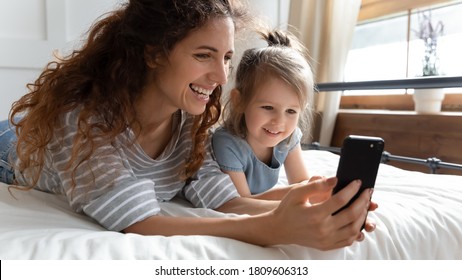 Close Up Nanny Show Cartoons On Smartphone To Little Kid Girl. Waking Up Lying On Bed Mom And Daughter Use Phone Make Videocall Enjoy Distant Talk With Relatives, Parental Control Modern Tech Concept