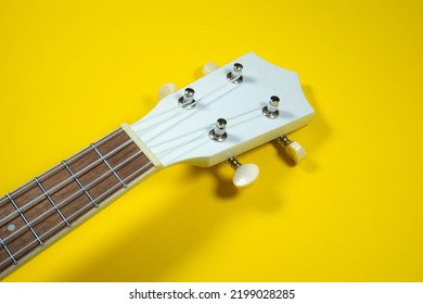 Close up neck of the guitar.
White colored wooden ukulele guitar on the yellow background. Hawaiian Four String Guitar. Musical Instrument.