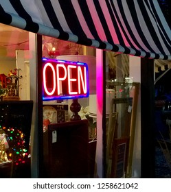 Close Up Of Neon Open Sign On The Exterior Of A Small Business Feature Christmas Holiday Items And A Black And White Awning