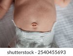 Close up of newborn baby belly and belly button in diaper, lying on white blanket. Baby navel, delicacy of newborn skin.