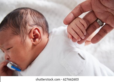 Close Up Of Newborn Baby In Cot Holding Parent's Finger