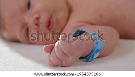 Close up of newborn baby with nametag bracelet. Infant lying in crib in hospital. New born baby first days of life in delivery room. Healthcare concept
