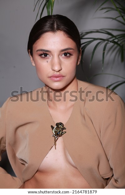 Close up non retouched image of brunette model\
with a big mole on her face, professional make up and up-do\
hairstyle. Unconventional beauty body positivism. Brown blazer\
decorated with pin brooch