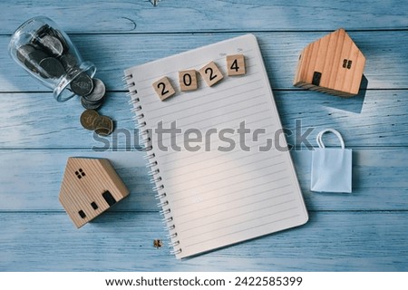 close up notebook, 2024 wooden text block, toy house, small shopping bag, glass bottle with coin on table, saving and manage money to success business, to do list and mission goal wallpaper background