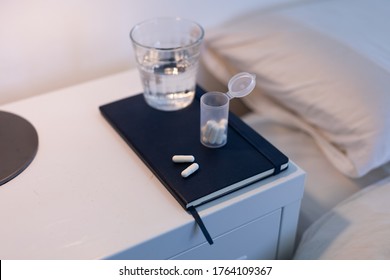 Close Up Of A Notebook, Box Of Tablets And A Glass Of Water Lying On A Cabinet Next To A Bed, Medication During Isolation Lockdown Against Covid 19 Coronavirus Pandemic 