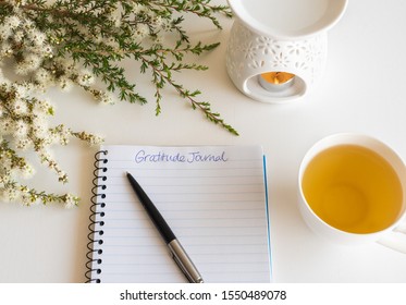 Close up of notebook and pen with handwritten Gratitude Journal text on table with oil burner and flowers (selective focus)