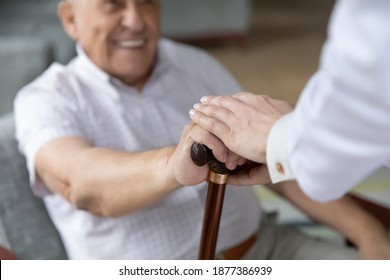 Close up of nurse caregiver palms covering hand of smiling senior patient holding cane. Sick old man struggle with trauma consequence make success on rehabilitation therapy with help support of doctor - Powered by Shutterstock