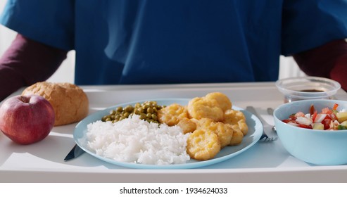 Close up of nurse carrying tray with hospital food for patient in hospital. Cropped shot of male prisoner holding tray with meal walking indoors
