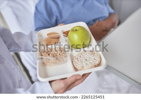 Close up of nurse holding healthy breakfast meal on tray and bringing in to patient in hospital