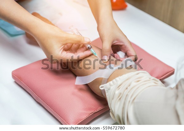 Close up nurse pricking needle\
syringe in the arm patient drawing blood sample for blood\
test