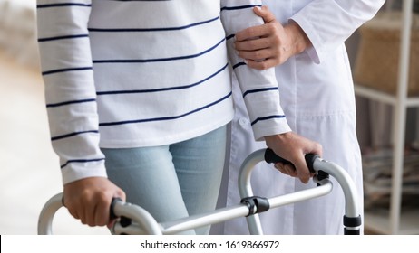 Close up nurse wearing white uniform helping disabled older woman to use walker, caregiver holding mature patient hand, rehabilitation and recovery after injury concept, healthcare and orthopedic