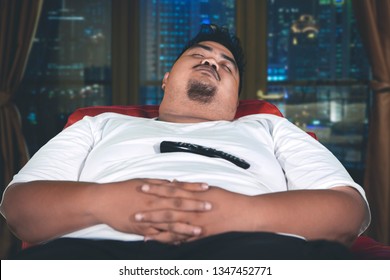 Close Up Of Obese Man Sleeping With A Remote Control On His Belly And Sitting On The Sofa