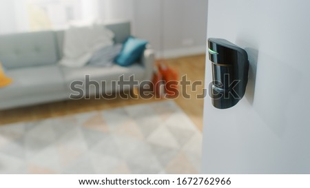 Close Up Object Shot of a Modern Movement Detector Unit on a White Wall in a Cozy Apartment in the Background.