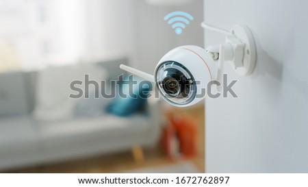 Close Up Object Shot of a Modern Wi-Fi Surveillance Camera with Two Antennas on a White Wall in a Cozy Apartment Has Wi-Fi Icon Above it.