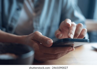 Close up of, woman sitting at wooden table using mobile phone in coffee shop, finger touching on phone screen. Woman using smartphone for mobile banking, online shopping, social media network