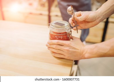 Close Up Og Hands Assistant Merchant Closing Glass Jar With Spice In Grocery Zero Waste Store Over Rack Counter. Sun Glare Copy Space.