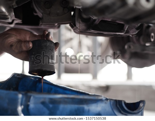 Close up Oil Filter. Professional car mechanic changing\
motor oil under car at the garage. Mechanic oil change service.    \
 