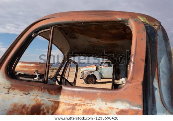 Close up of old\
antique rusty truck door with second rusty vintage truck in distant\
and overcast sky, Africa