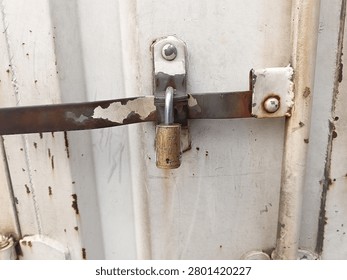 Close up of old brass padlock locking metal sliding latch bar on weathered cargo container door
