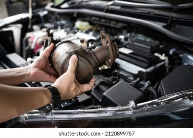 Close up old catalytic converter in hand Car service staff remove from engine gasoline car dust clogged condition on filter in service concept and engine room in the background - Shutterstock ID 2120899757