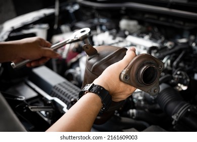 Close Up Old Catalytic Converter In Hand Car Service Man And Holding A Wrench For Remove Part In Engine Room Of Car , Service And Maintenance Concept In Garage