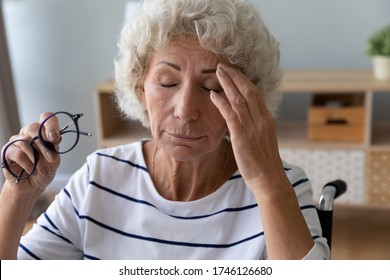 Close Up Old Disabled Woman Sit In Wheel Chair Taking Off Glasses Closed Eyes Reduces Eyestrain Suffers From Headache Feels Exhausted. Poor Vision, Age-related Eye Problems, Glaucoma, Dry Eyes Concept