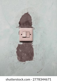 Close up of an old double light switch mounted on a weathered wall with peeling paint, cracks, and patch repair marks. 