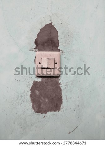 Close up of an old double light switch mounted on a weathered wall with peeling paint, cracks, and patch repair marks. 
