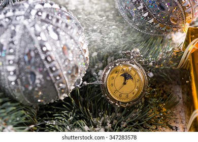 Close Up Of Old Fashioned Pocket Watch Hanging On Snow Covered Sprigs Of Evergreen Tree Decorated With Sparkling Silver Christmas Balls