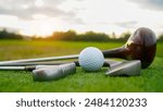 Close up old golf club and golf ball on green grass with sunset background. Golf ball and wooden driver on green grass background.                                