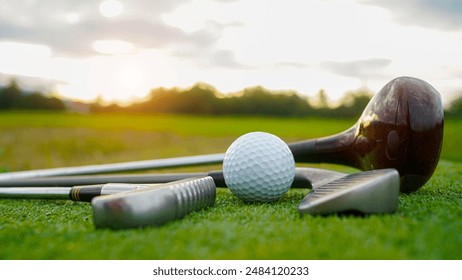 Close up old golf club and golf ball on green grass with sunset background. Golf ball and wooden driver on green grass background.                                 - Powered by Shutterstock